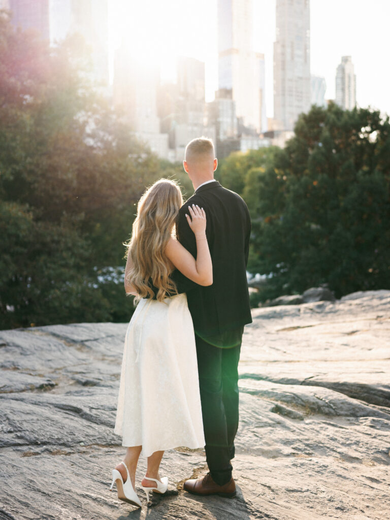 A bride and groom look at the Midtown Manhattan skyline from the scenic rocks in Central Park during a sunset photoshoot.