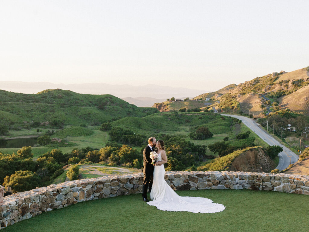 A bride and groom kissing on the scenic overlook at Cielo Farms wedding venue in Malibu, surrounded by rolling green hills.