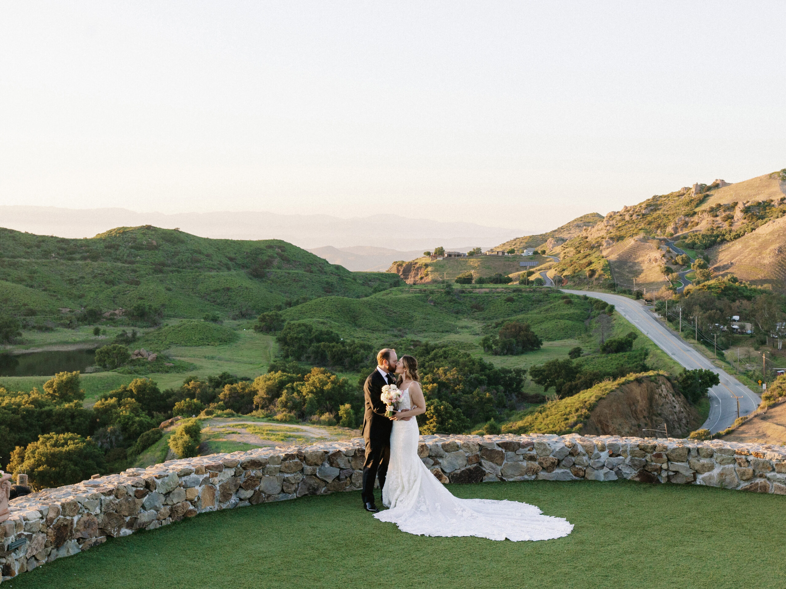 A bride and groom kissing on the scenic overlook at Cielo Farms wedding venue in Malibu, surrounded by rolling green hills.