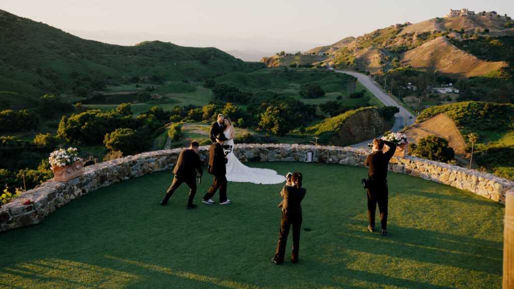 Professional cinematic wedding videographers and editorial photographers shooting a luxury bride in a couture gown during a scenic sunset session.