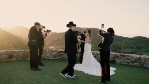 Behind-the-scenes of a luxury media production team filming a bride and groom on the panoramic stone terrace at Cielo Farms in Malibu.