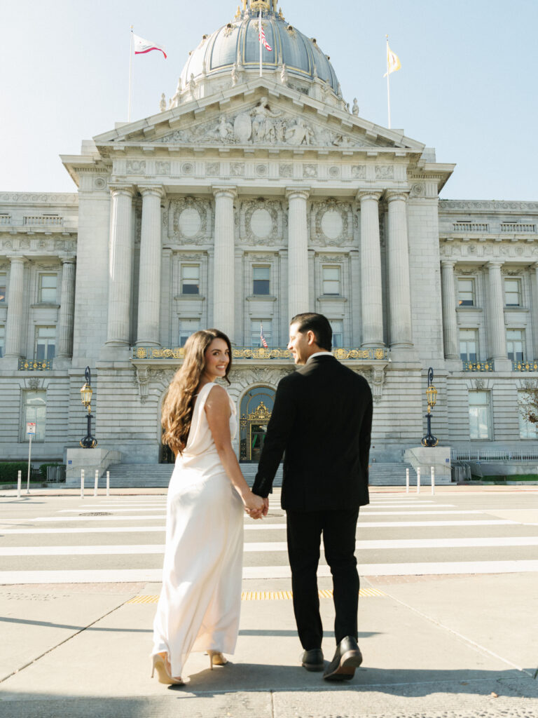 Editorial wedding photography of a couple walking away against the grand beaux-arts facade of San Francisco City Hall.