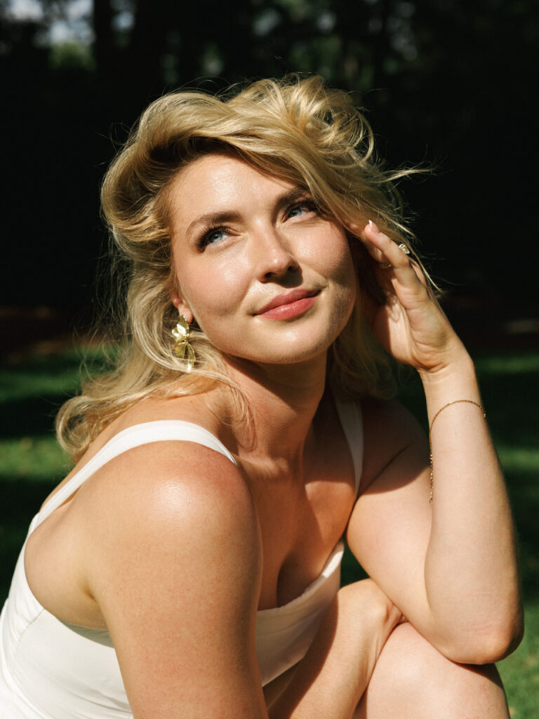 Sun-drenched bridal portrait showcasing a blonde bride with an old Hollywood wave hairstyle, wearing statement gold earrings and a white dress.