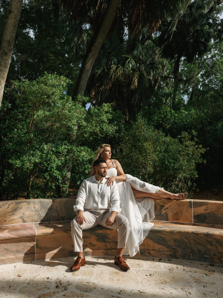 Bride in a white maxi dress with a slit and groom in a linen shirt posing outdoors for a tropical rehearsal dinner style gallery.