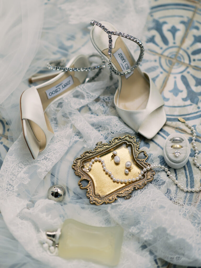 Luxury California wedding details featuring silk Jimmy Choo bridal shoes with crystal straps on fine lace fabric.