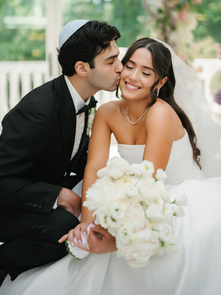 A groom wearing a yarmulke kisses his bride during a luxury Jewish wedding celebration at a New York estate.