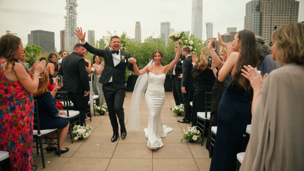 A joyful bride and groom celebrate during their wedding recessional on a luxury Manhattan rooftop terrace with skyline views.