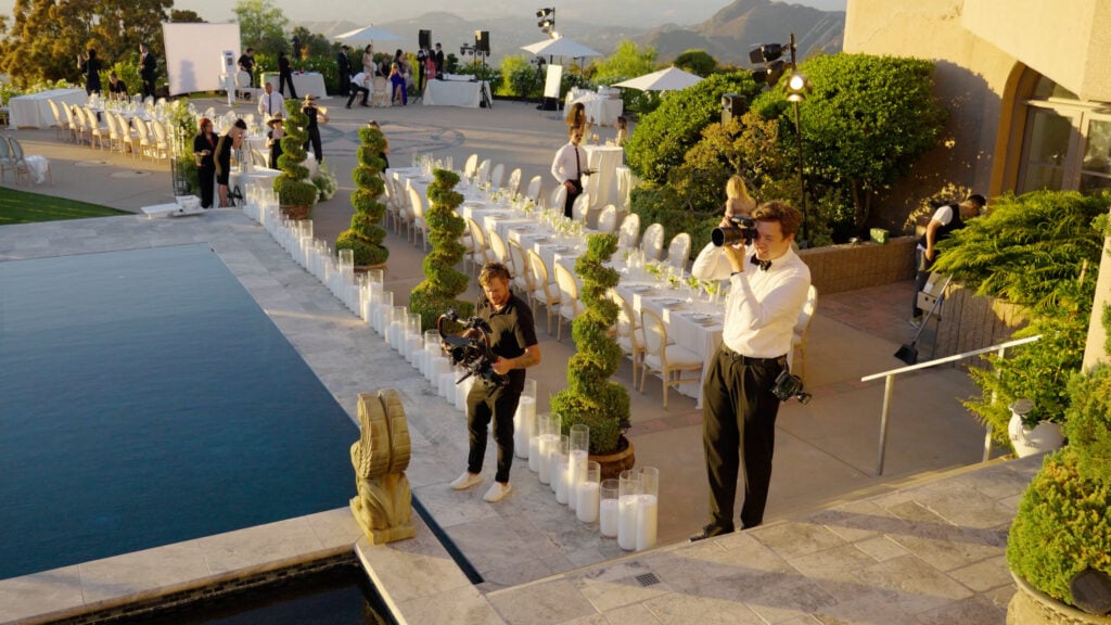 Behind-the-scenes of a luxury wedding production crew capturing an opulent poolside reception setup at a private Malibu cliffside estate.