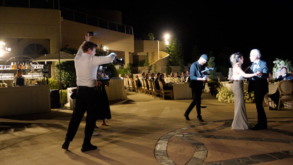 Professional wedding videographers capturing the father-daughter dance under artificial spotlights at a luxury outdoor reception at Cielo Farms.