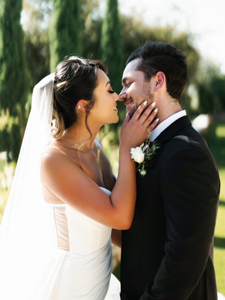 Close-up portrait of a bride gently touching her groom's face before a kiss during a wedding photo and film portrait session at Greystone Mansion.