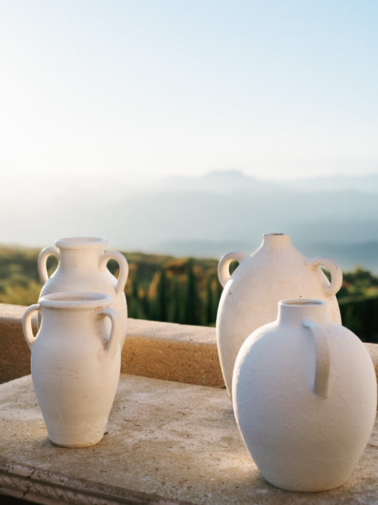 Minimalist luxury wedding decor featuring textured ceramic vases on an outdoor terrace ledge overlooking a panoramic mountain landscape.