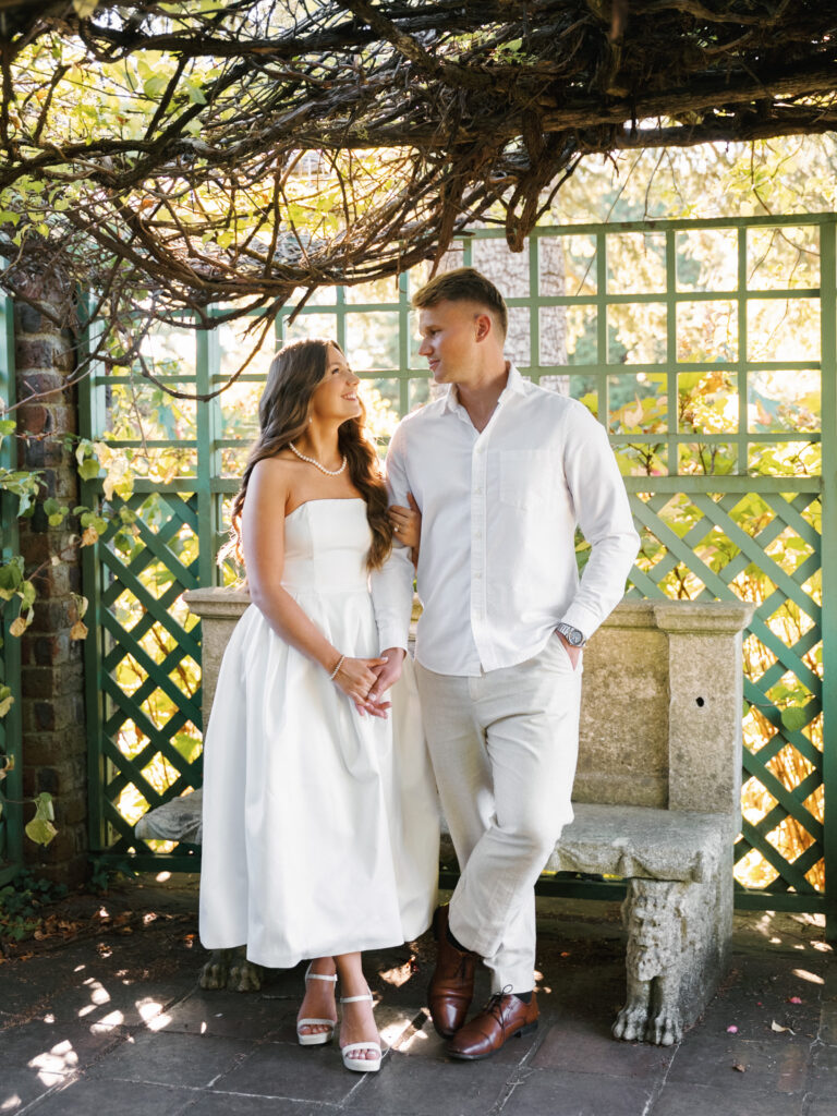 Elegant couple holding hands in a formal estate garden, showcasing sophisticated outdoor engagement or rehearsal dinner attire.