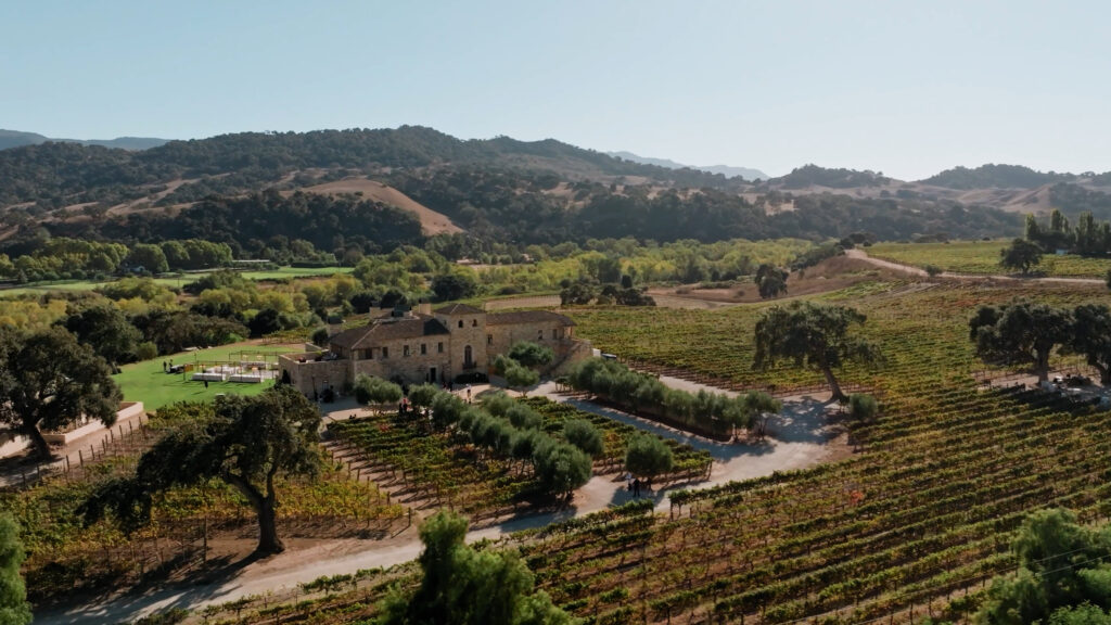 Cinematic aerial view of Sunstone Winery and Villa in Santa Ynez, a luxury European-style destination wedding venue in California surrounded by sun-drenched vineyards.