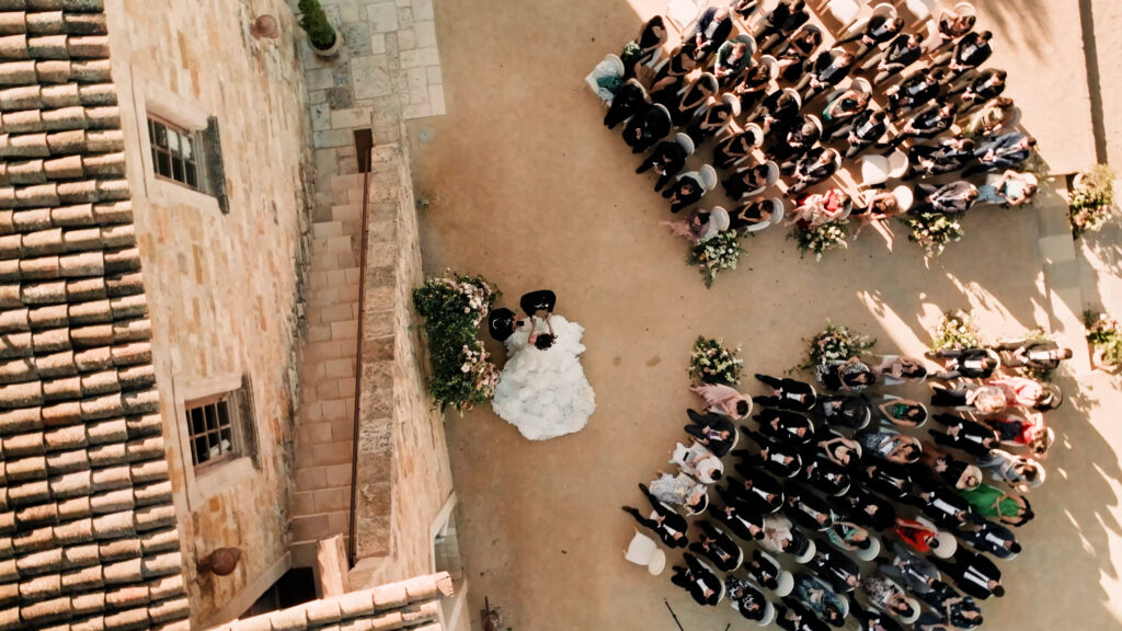 Bride and groom at their outdoor wedding ceremony at Sunstone Villa, showcasing a unique curved guest seating layout next to the historic stone winery building.