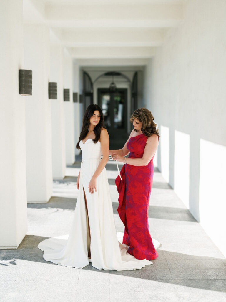 Editorial wedding photograph of a mother helping the bride adjust her dress during getting ready moments.