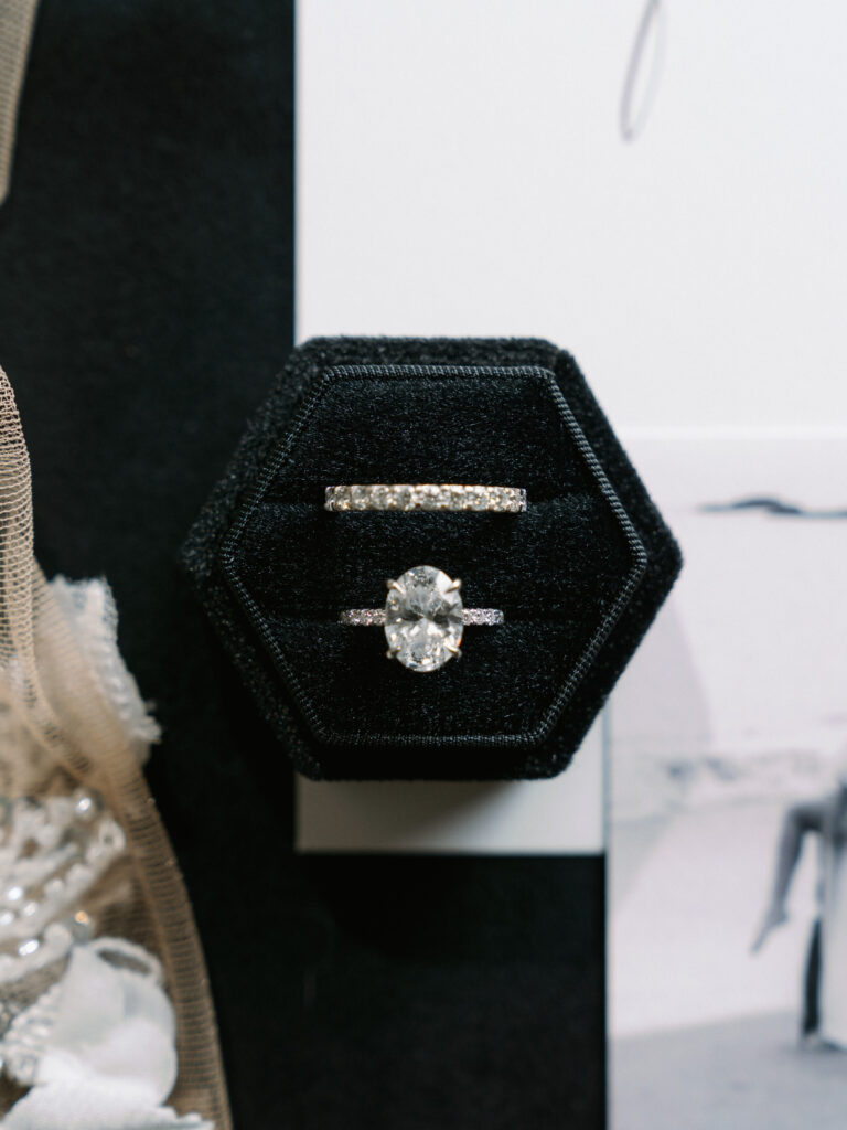 Oval cut diamond engagement ring and matching pavé wedding band inside a black hexagon velvet ring box.