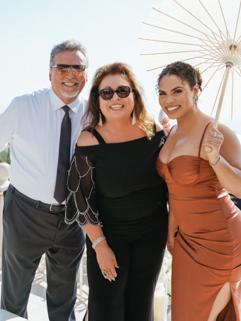 Sophisticated wedding guests in chic attire holding a white parasol umbrella, high-fashion summer estate wedding inspiration.