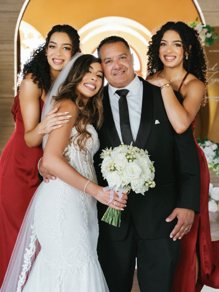 Elegant bride holding a white rose bouquet posing with family at a luxury venue, emotional documentary wedding video story inspiration.