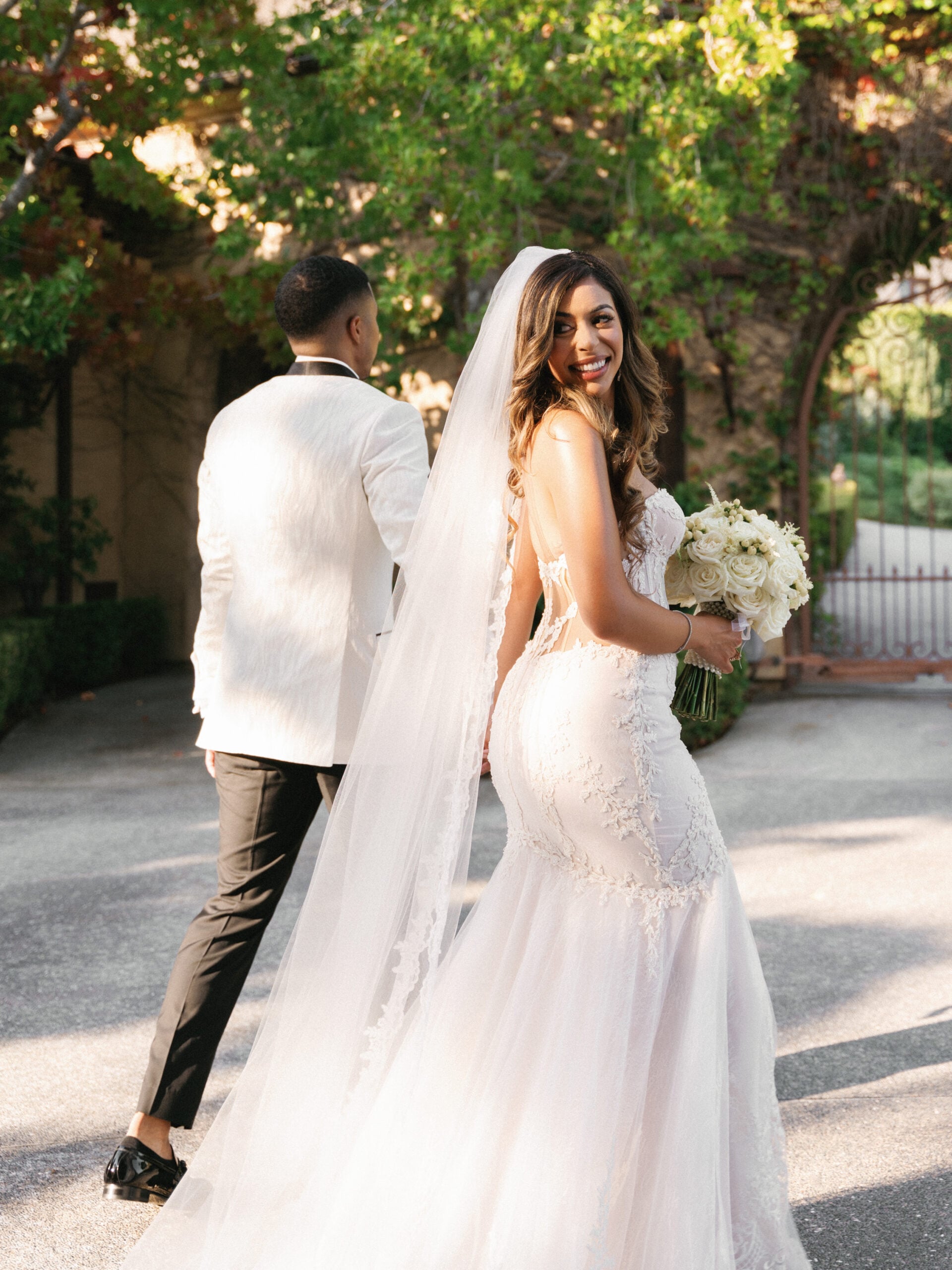Documentary vs cinematic wedding video guide concept with a luxury bride in a lace mermaid gown looking back, elegant couple walking at a private estate.