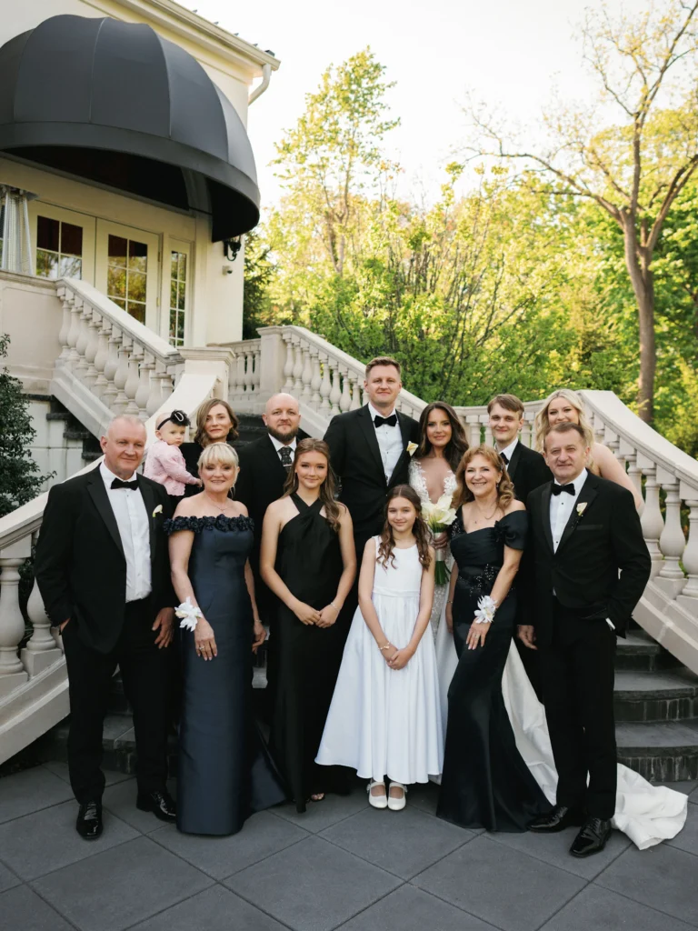 A formal family wedding portrait with a bride, a groom, and their parents standing and smiling directly at the camera during a post-ceremony photo session.