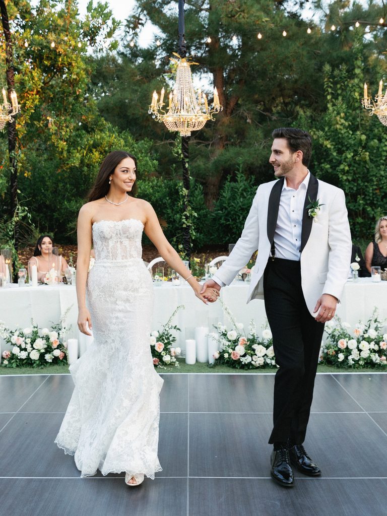Newlyweds walk hand-in-hand onto an outdoor dance floor, captured in elegant wedding reception photos.