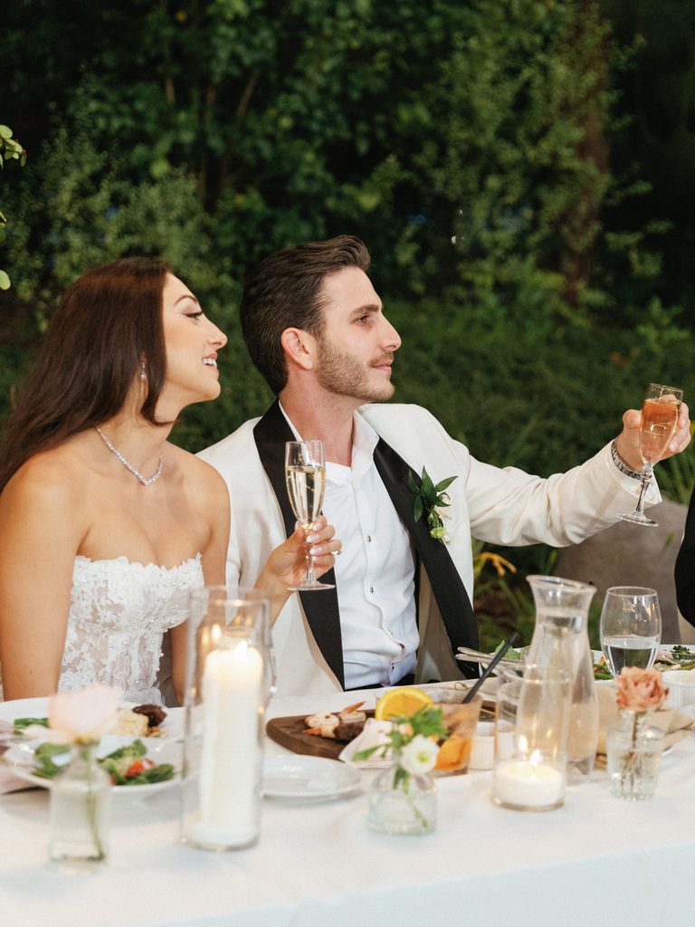 Newlyweds raise a glass at their sweetheart table while listening to touching speeches in these emotional wedding reception photos.