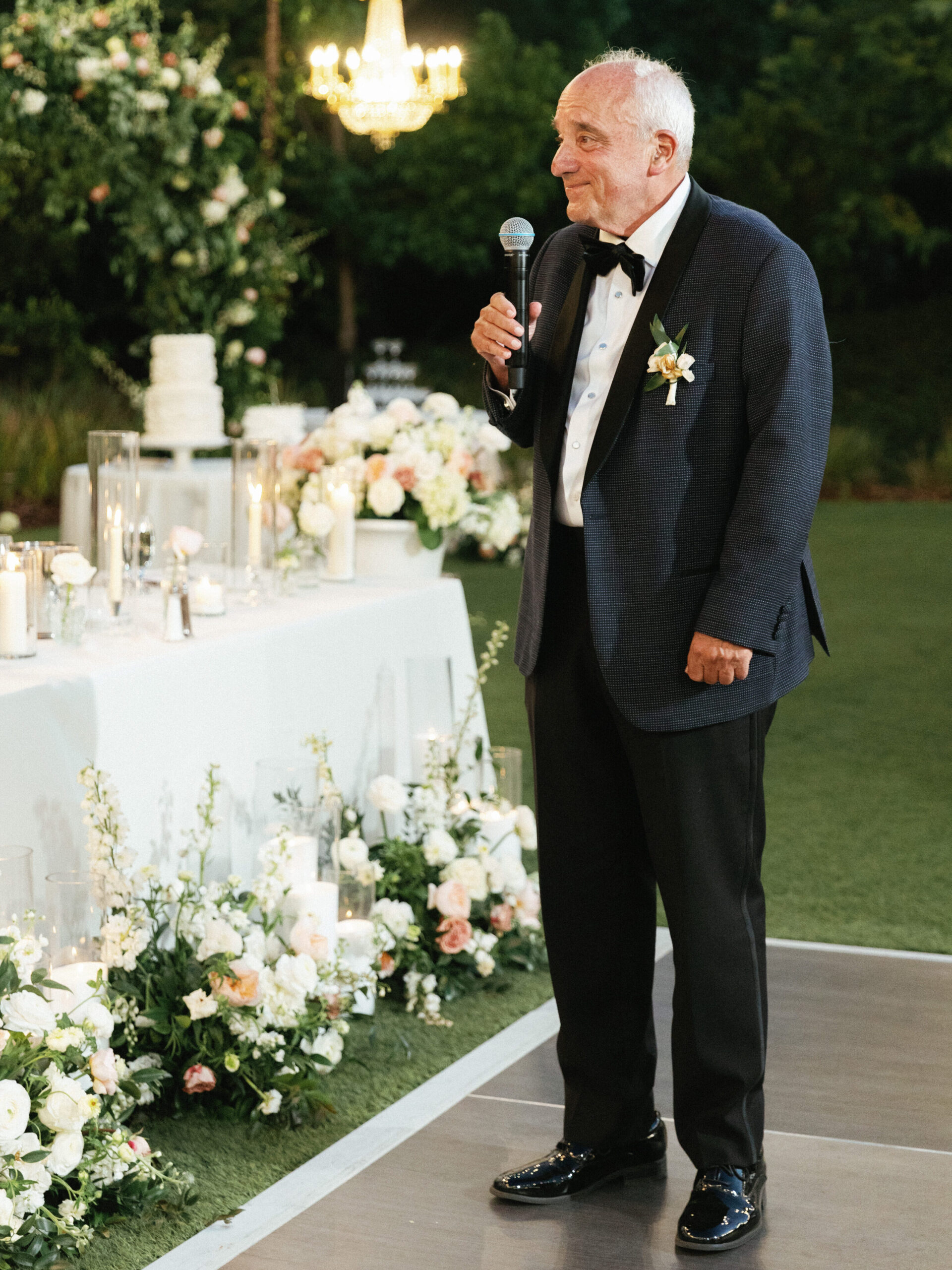 Grandfather of the bride holds a microphone and gives a heartfelt toast during a luxury outdoor celebration.