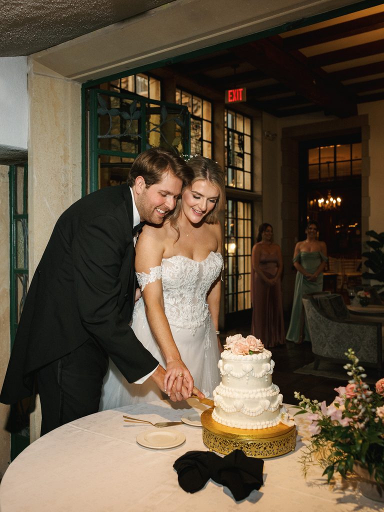Bride and groom cutting a vintage wedding cake under elegant reception lighting inside a luxury venue.