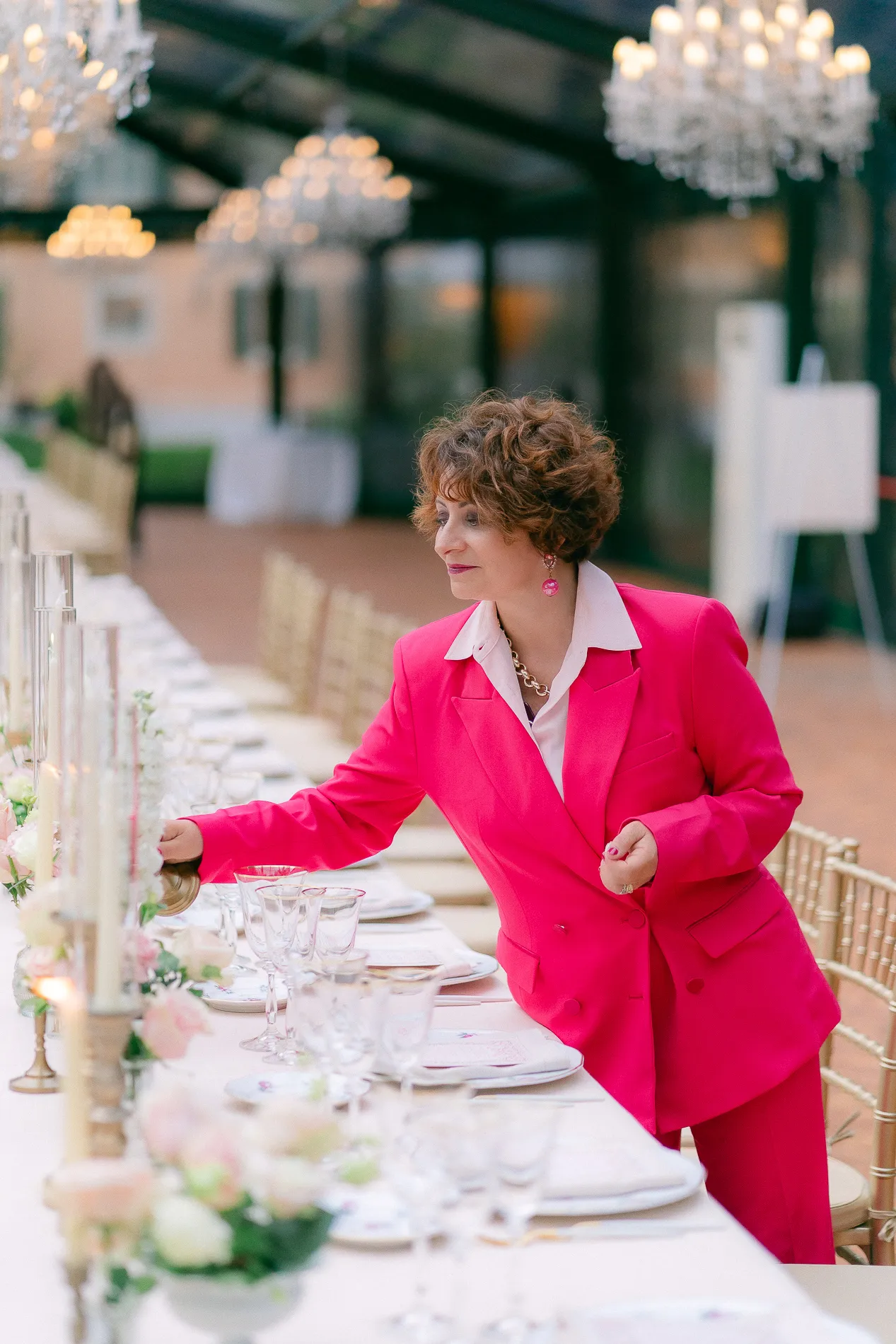 Wedding planner in a pink suit arranging table settings at a wedding