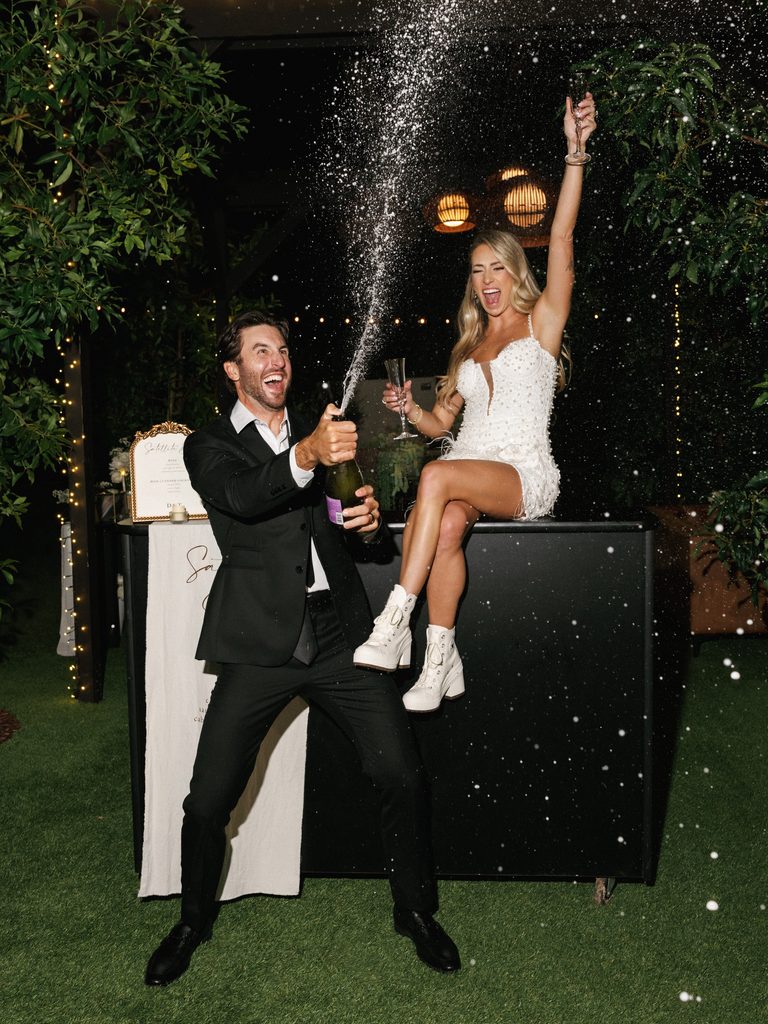 Joyful groom spraying champagne with the bride during a high-energy luxury wedding reception.
