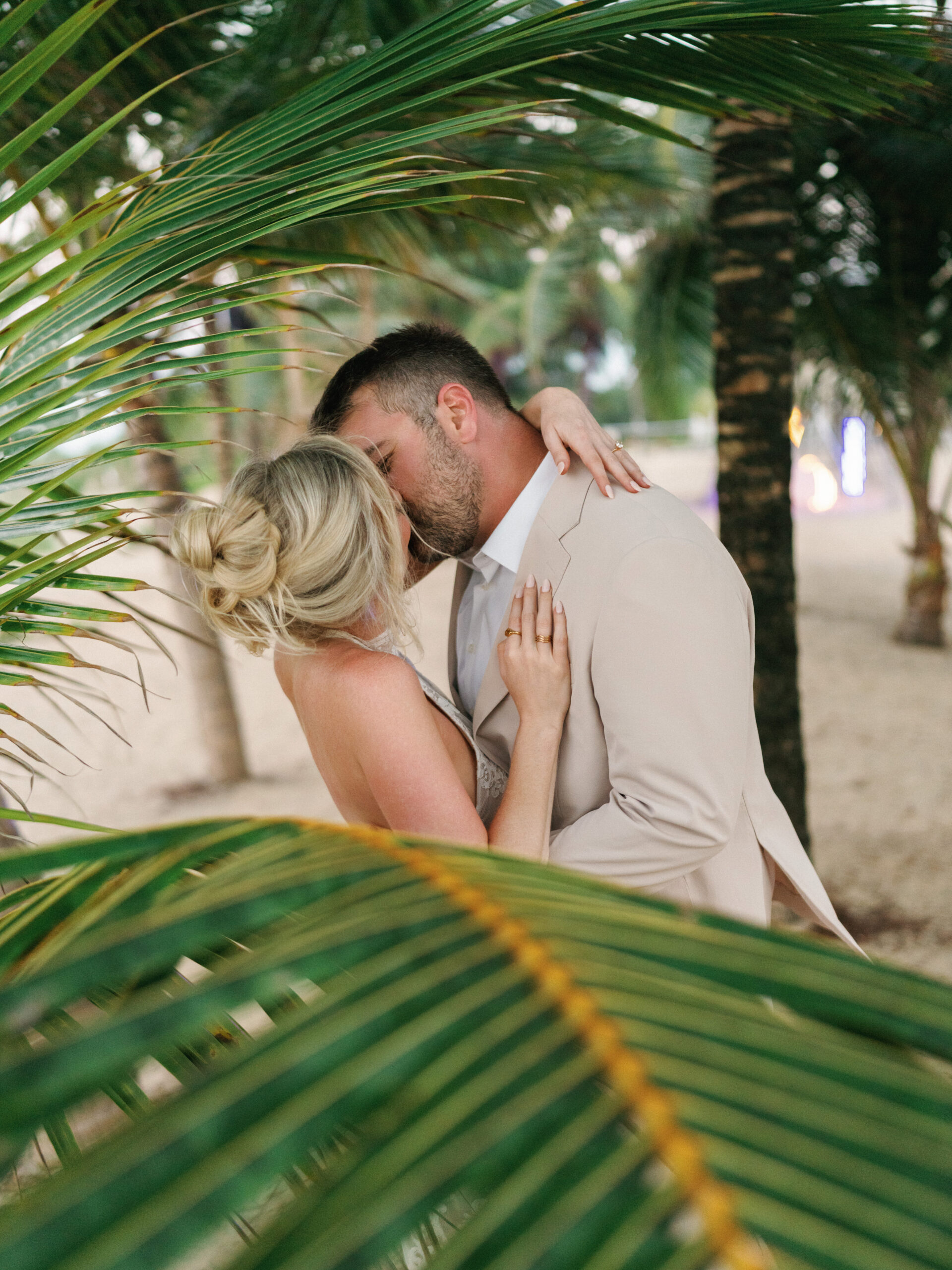 Cinematic bride and groom sharing a beach kiss framed by vibrant exotic palm trees