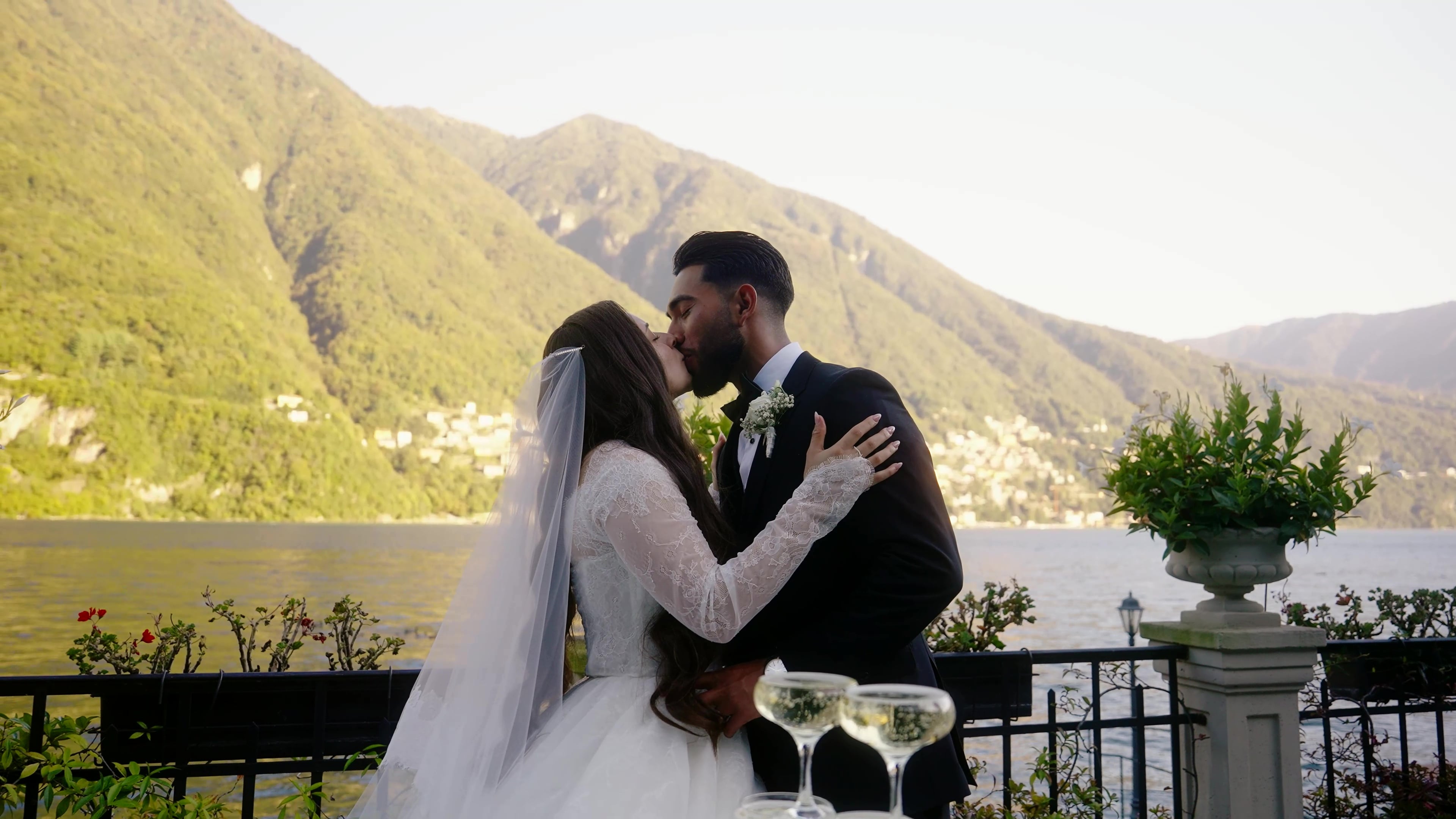 Wedding couple kissing with Italian mountains in the background and champagne glasses
