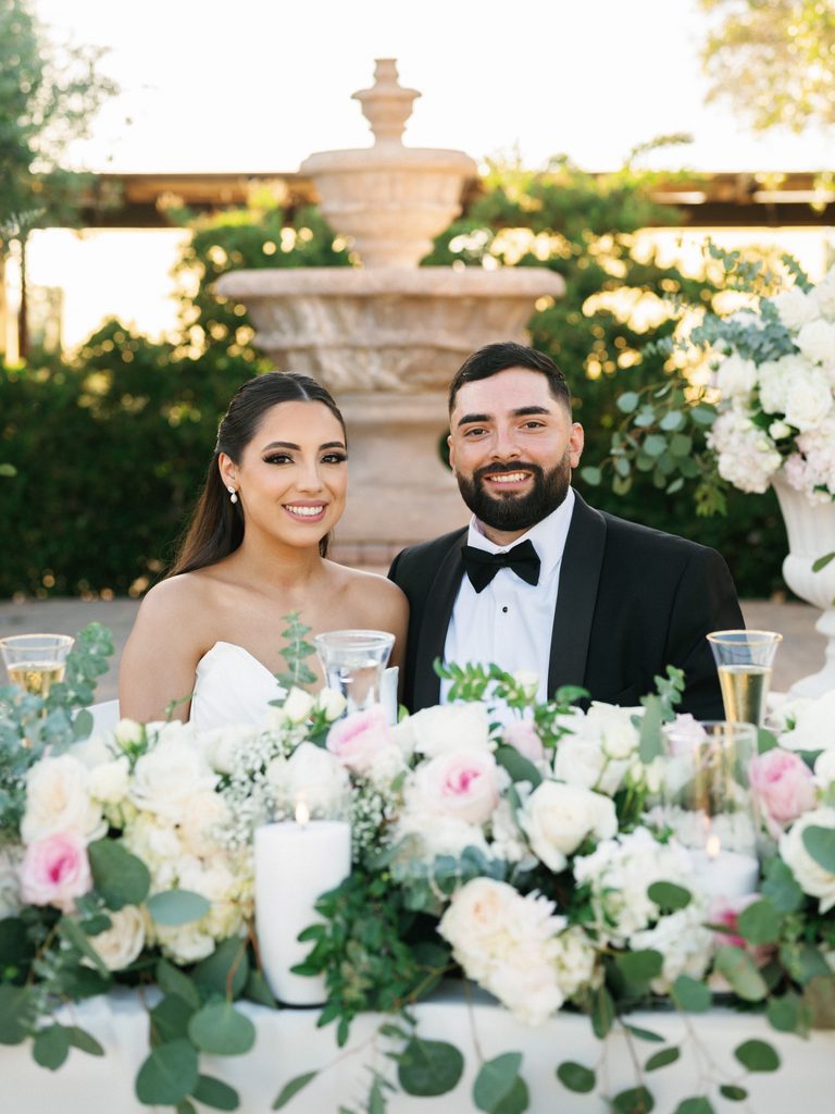 Bride and groom smile beautifully at their floral sweetheart table in these elegant wedding reception photos