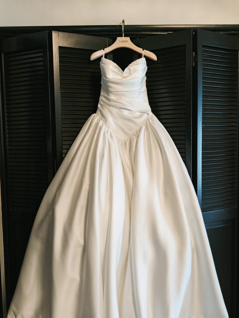 Luxury white satin ballgown hanging on a dark wooden screen during bridal prep