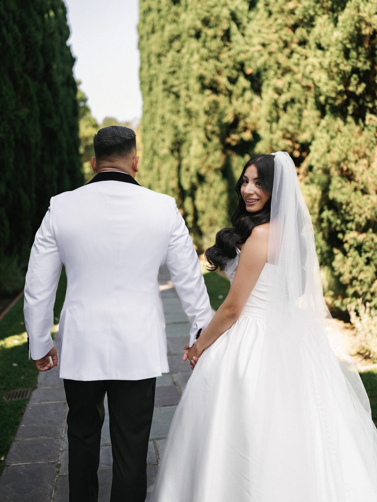 Beautiful bride looking over her shoulder while walking hand in hand with her groom