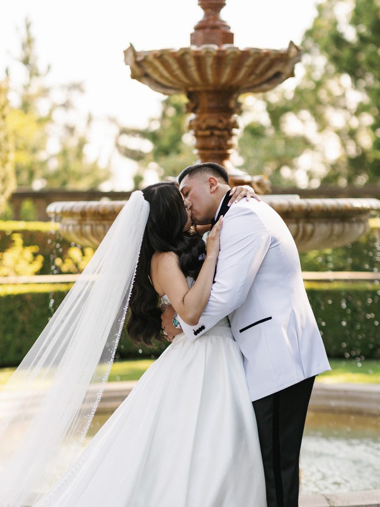 Groom in a white tuxedo jacket embracing his bride during outdoor vows
