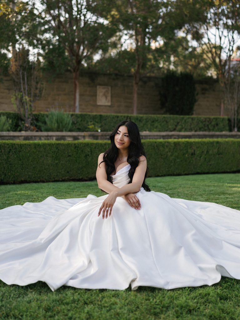 Beautiful bride sitting on a manicured green lawn showing her huge satin ballgown train