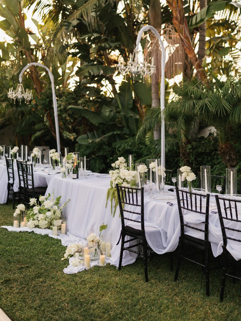 Outdoor head table design featuring black Chiavari chairs against a tropical garden backdrop