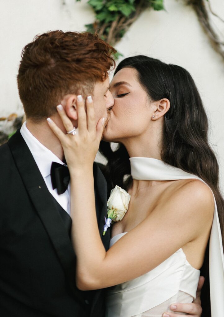 Intimate close-up of a bride and groom kissing against an ivy wall backdrop, showcasing romantic and organic wedding photography styles.
