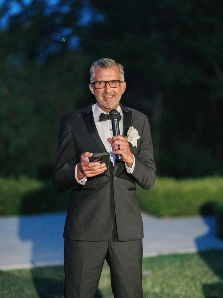 Father of the bride giving a speech during an outdoor wedding reception with soft evening lighting.