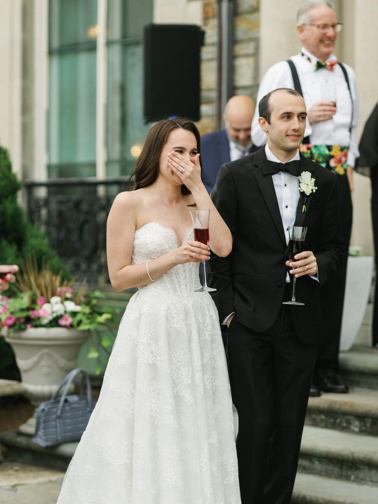 Emotional bride and groom listening to outdoor wedding reception speeches in soft daylight.