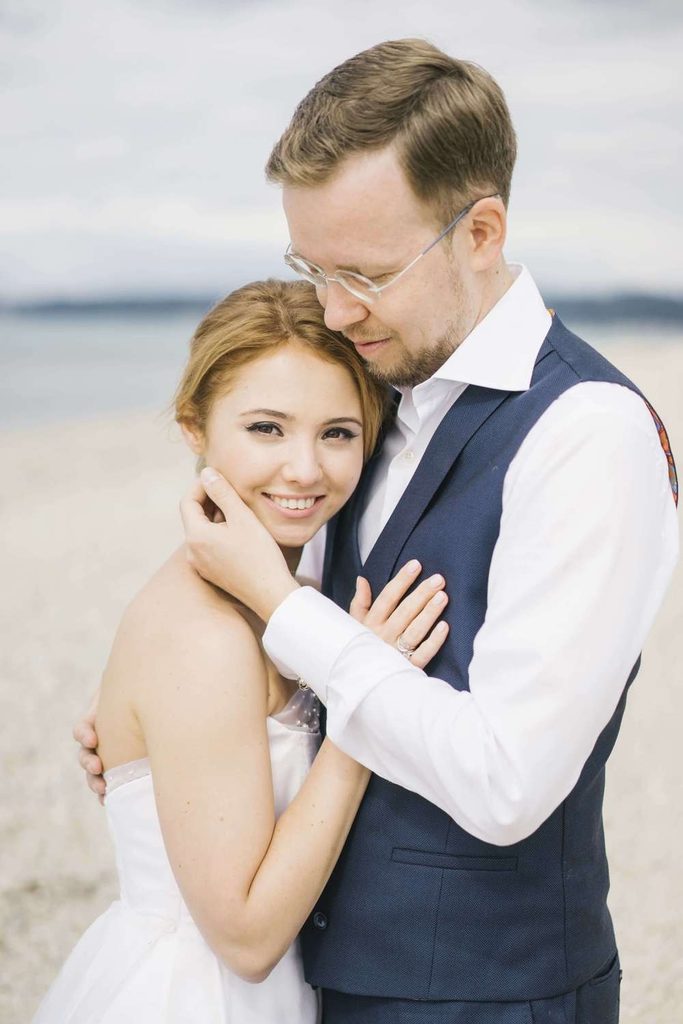 Loving groom embracing his smiling blonde bride on a sandy ocean shore