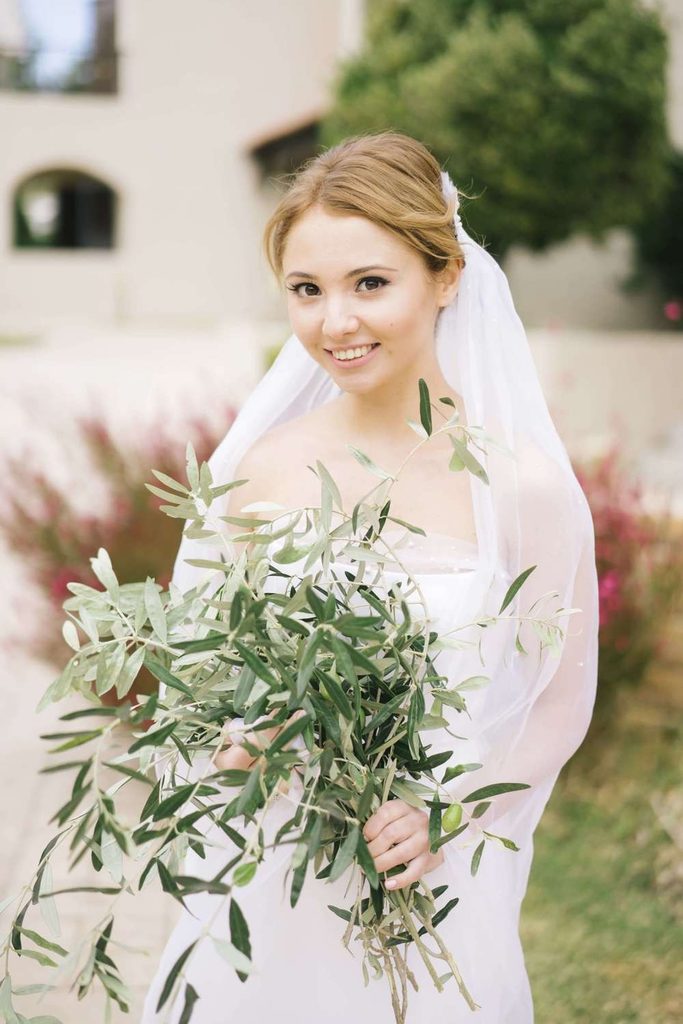Beautiful bride holding an organic olive branch bouquet near a Mediterranean villa