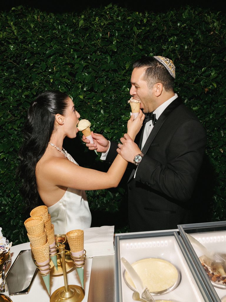 Newlyweds feed each other ice cream cones at a late night dessert station during their luxury wedding reception