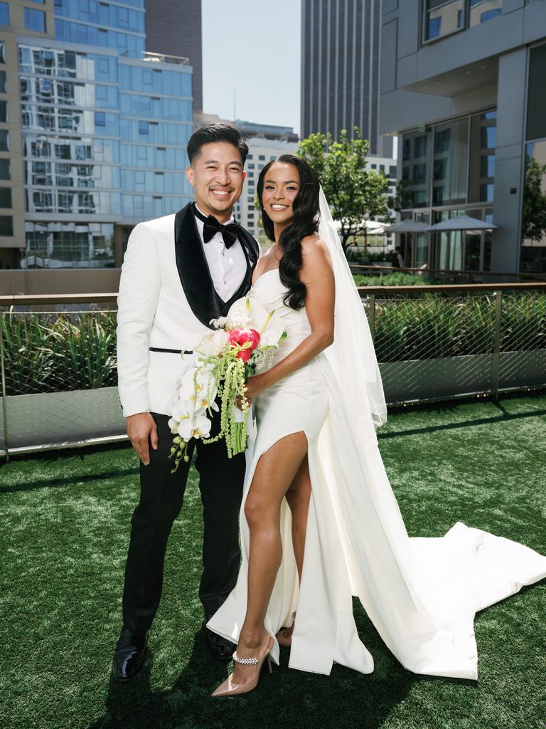 Chic city newlyweds with an orchid cascade bouquet posing against a downtown skyscraper backdrop.