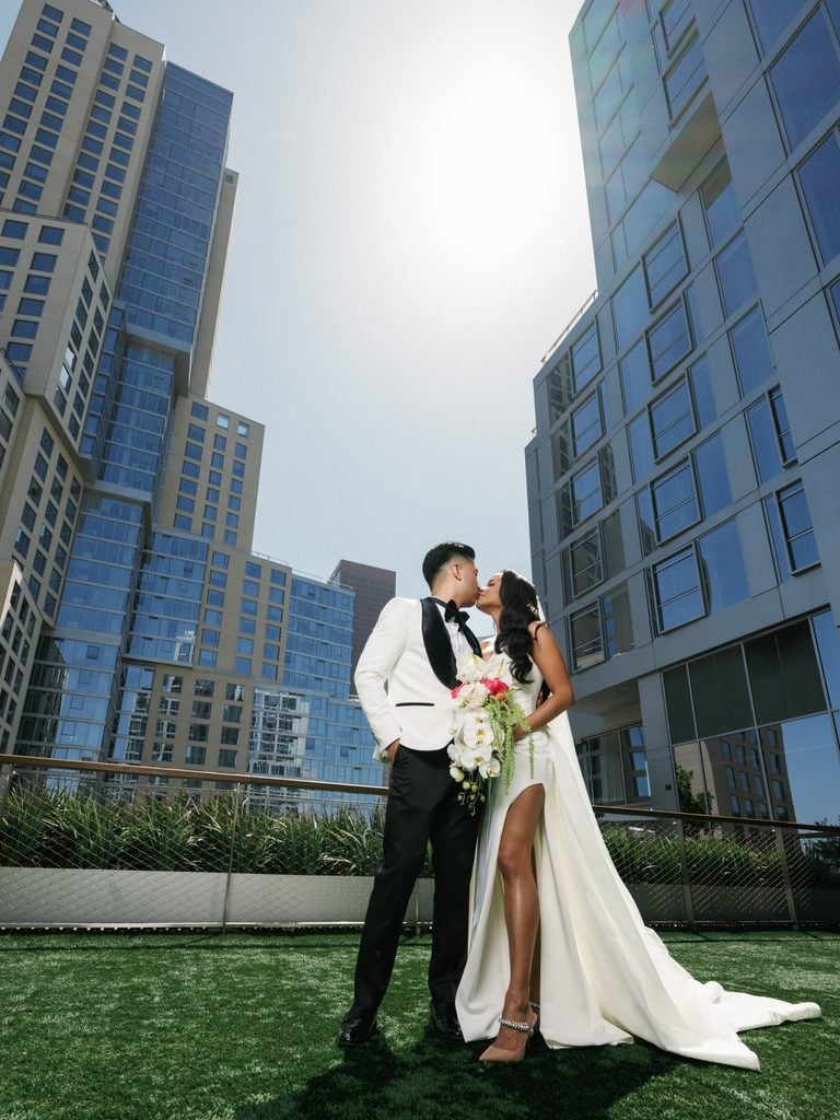 Newlyweds sharing a romantic kiss on a rooftop terrace surrounded by modern glass skyscrapers, showcasing contemporary urban wedding photography styles.