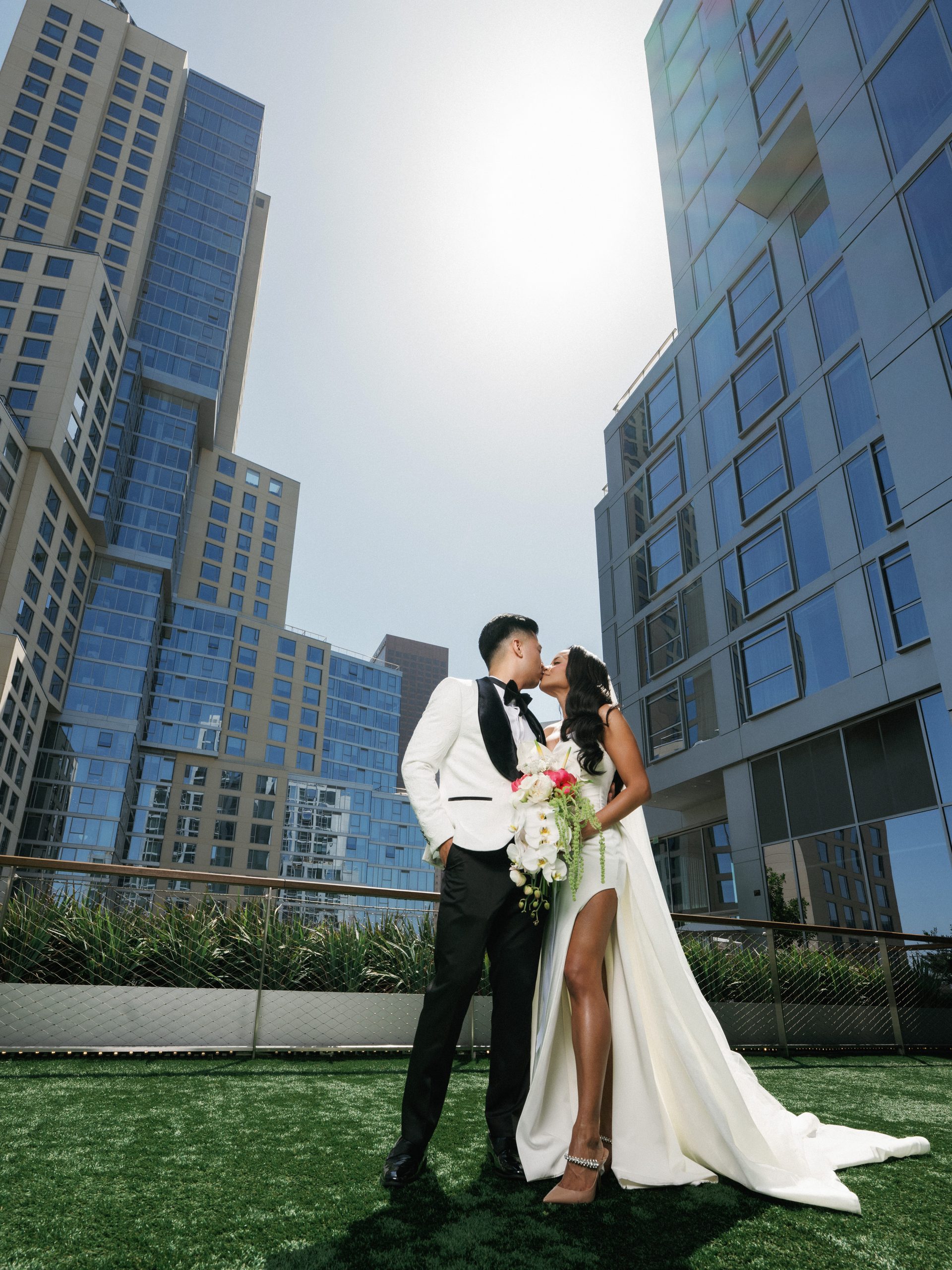 Newlyweds sharing a romantic kiss on a rooftop terrace surrounded by modern glass skyscrapers, showcasing contemporary urban wedding photography styles.