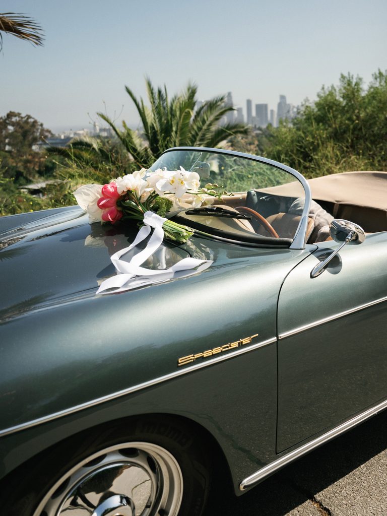 Luxury wedding bouquet with white orchids resting on a vintage green Porsche Speedster with the LA skyline in the background.