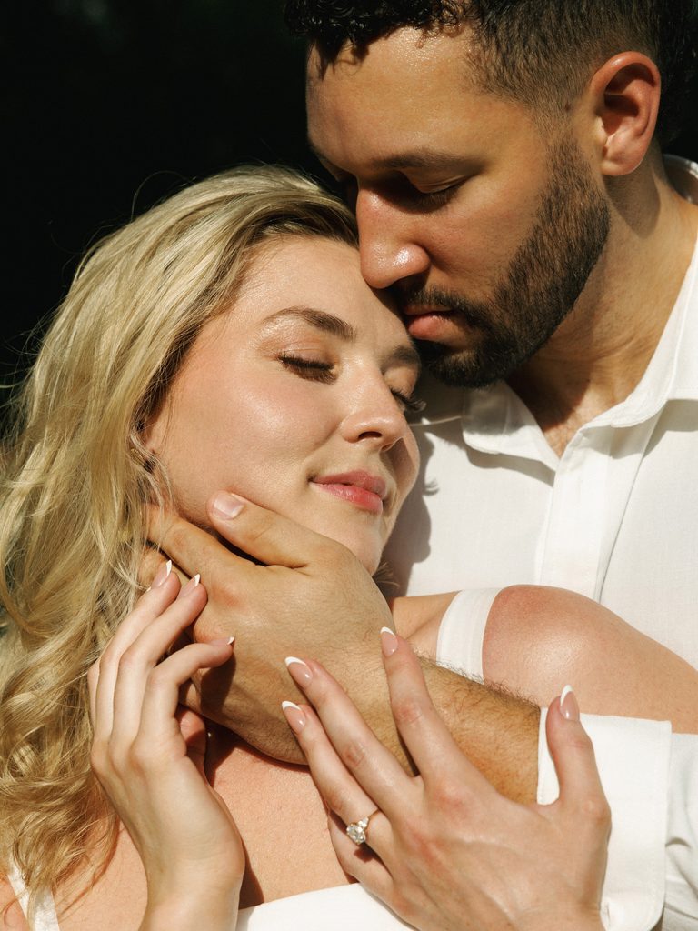 Groom tenderly touching his brides face during a sunny outdoor photoshoot