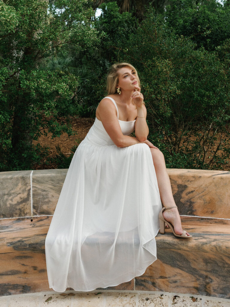 Thoughtful bride in a flowing white gown posing outdoors under natural light